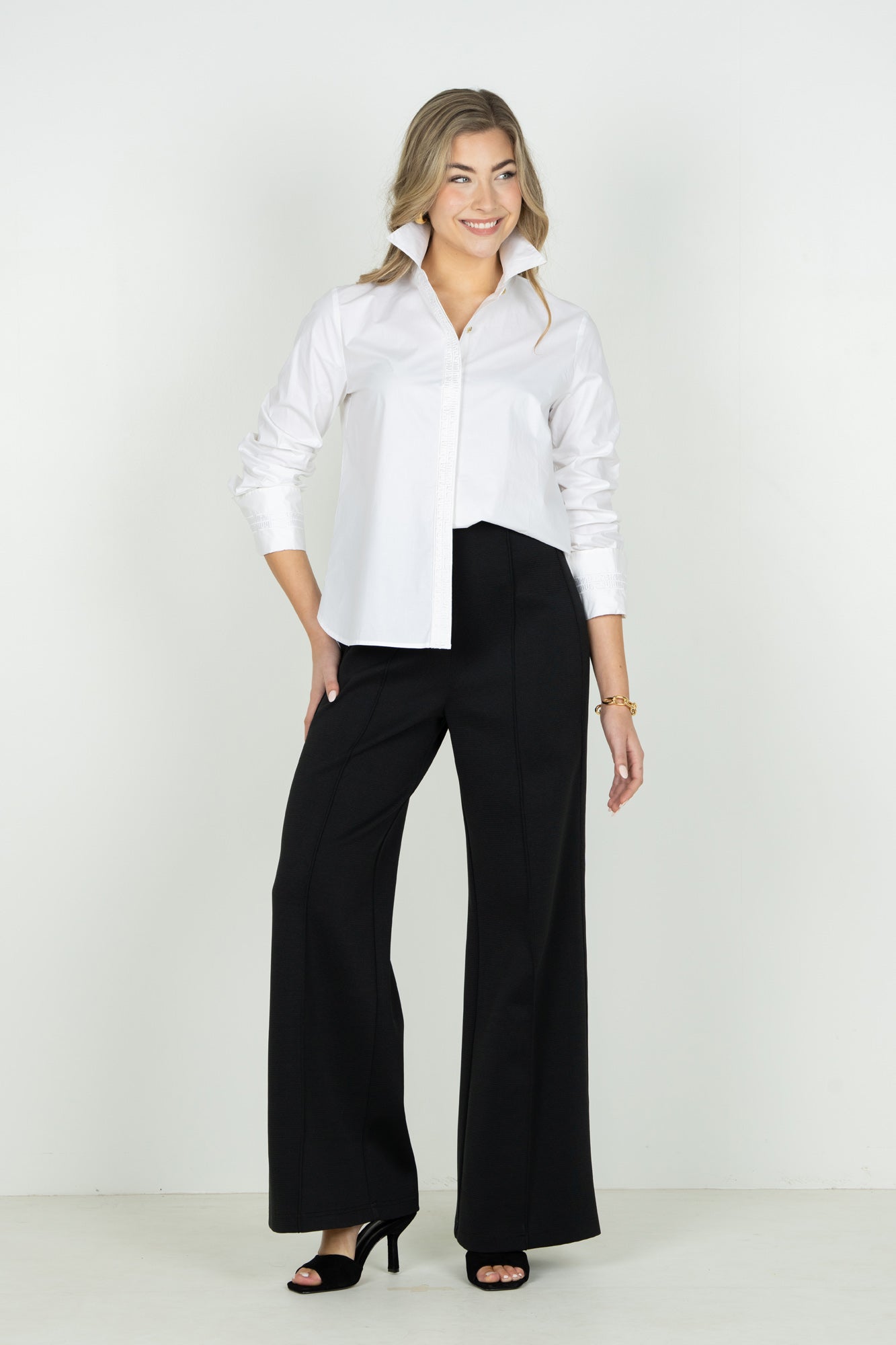 Woman wearing white classic oxford button-down shirt with black wide-leg trousers and heels.