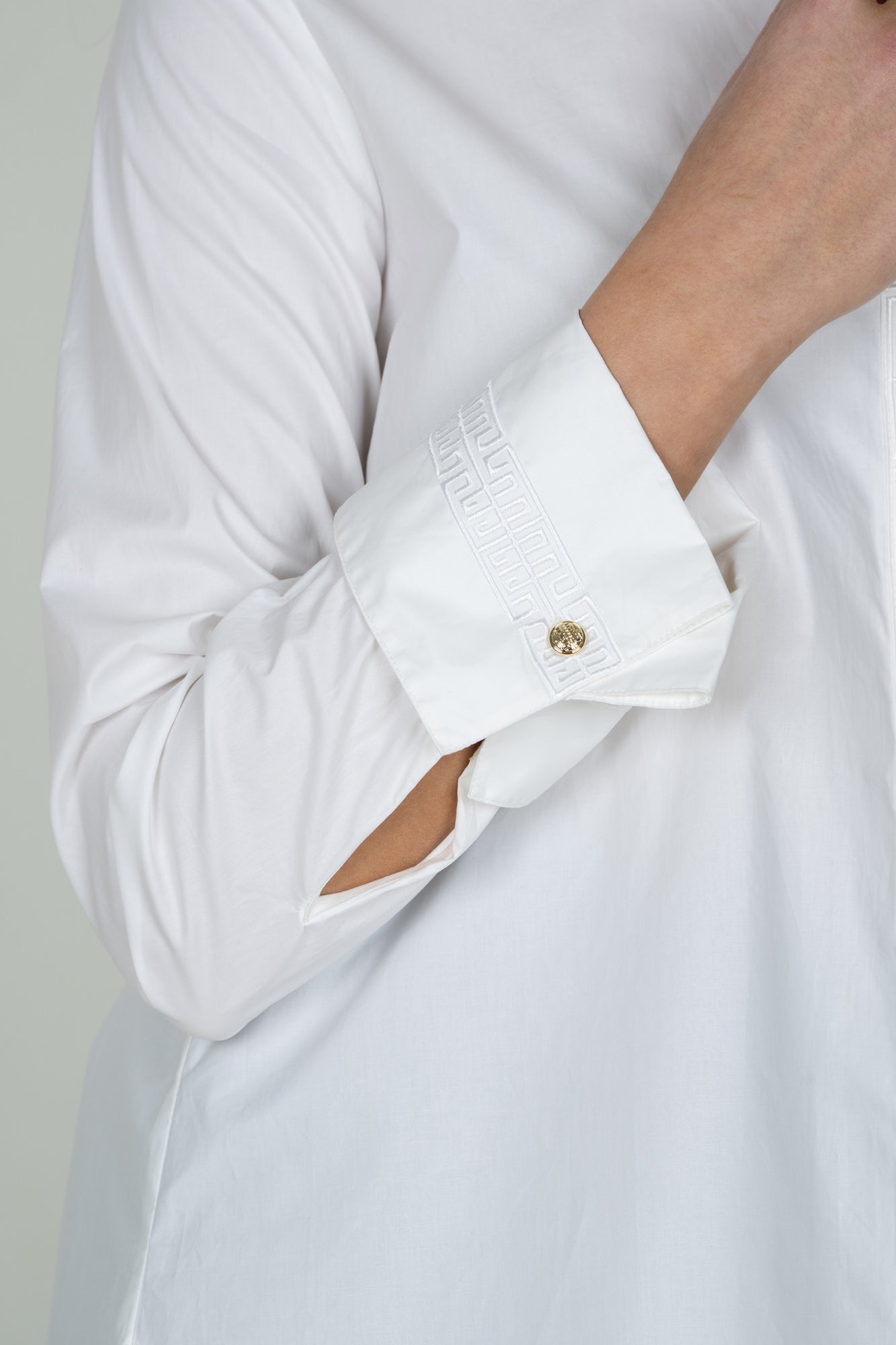 Close-up of white Oxford shirt cuff with embroidered Greek key detail and gold button